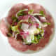 The salad is arranged on top of the salami bed.