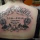 The name and years lived of a loved one are tattooed on the wearer's upper back.