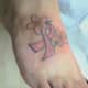 Pink ribbon tattoo with flower element on foot.