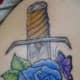 This sword tattoo features a blue rose and a butterfly.