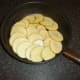 Potato slices are carefully arranged in a deep frying pan