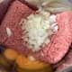 Ground pork and beef meat in a bowl with eggs, onion, and garlic