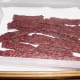 Deer jerky all done and cooling down on paper towels. You can dab the shiny grease spots off to help it dry and cool.