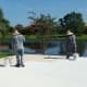 The two men are applying paint using long roller brushes.