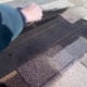 The upper shingle is pried high, showing the roofing paper under it. The broken shingle has been completely removed. Note the staples that need removed.