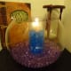 A vase of blue water beads with a candle within a larger bowl of purple beads.