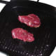 Kangaroo steaks are laid in smoking hot griddle pan