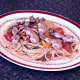 Spaghetti and vegetables are plated with frogs' legs on top