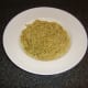 Spaghetti and green pesto sauce is laid in the bottom of a deep serving plate