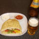 Curried chicken burger in naan bread is served with a glass of Indian beer.