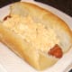 Egg mayo is spooned on to bacon dog