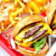 Two delicious INO burgers; the left looks to be a 3x3 (three meat, three cheese) and the right is a single cheeseburger, both with "stock" ingredients: lettuce, tomato, onion (3x3 has grilled onion) and spread.