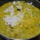 Step six: The bottle gourd and mung beans are almost cooked. Add grated coconut, turmeric powder, jaggery powder, and remaining salt. Mix well.