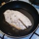 Floured tilapia fillet is laid in medium hot frying pan