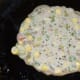 Heat a pan for the pancakes and grease it with some oil or ghee. Pour about one and a half ladles full of batter in the center and spread it a little.