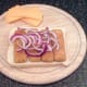 Onion strands are arranged on fish fingers on bread