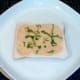 Houmous is spread on bread and garnished with shredded basil