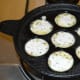 Heat a paddu pan. Add 1/4 tsp oil to each of the depressions. Cover the pan. Cook both of the sides until they are golden brown.