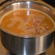 Step five: Take horse gram water in a sauce pan. Add spice paste, turmeric powder, jaggery, chopped onions, salt, and some hing. Add water as per instructions.