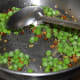 Step three: Add oil into a deep-bottomed pan. Throw in the mustard seeds. Let them crackle. Add split chickpea and white lentils. Saute until they turn golden brown. Add green peas. Saute for 2-3 minutes.