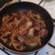 Chopped cooked sausages are added to pan with spiced onion and tomatoes