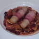 Chicken sausages in bacon are served on spicy beans bed