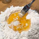 With a fork, lightly beat the eggs, gradually pulling flour from the inner rim of the well into the egg, until a soft, clumpy dough begins to form.