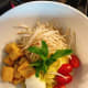 In a serving bowl, assemble the noodles, hard-boiled egg, fried tofu, tomatoes, mint leaves, and bean sprouts.