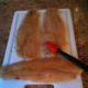 Basting the flounder fillet with teriyaki sauce.