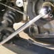 D. To loosen the crankshaft pulley bolt, secure the 22 mm socket to the bolt (upper right) and brace the breaker bar against the lower control arm (lower left).