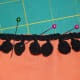 Adding some pom pom lace to a quilt top using the sewing machine. Pin the pom pom lace to the fabric, lining up the edge of the lace to the edge of the fabric.