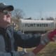 Moore hosing the contaminated water of Flint on the Governor's front lawn.