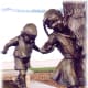 Partial view of a sculpture where 5 children are balancing themselves as they make their way across a log.
