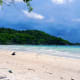 A kid lying on the beach cocks his head toward the sea.