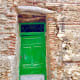 A bright-green, old entrance door to a building where people once lived.