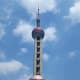 The Oriental Pearl Tower against a blue sky. A high-speed elevator shoots customers to the top of the tower where they can take in the views of the city.