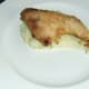Chicken leg is laid on the mashed potato and plate is ready for the peas
