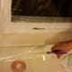 Apply shrink wrap to the window along the path of the adhesive tape, leaving about five inches of overhang. Then cut off the overhang.