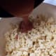 Pour flavor on popcorn in a bowl.