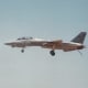 An F-14 with its wings extended, landing gear and tail hook down.