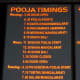The board displays Pooja details with time schedule.