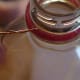 Close up of insertion of the wire hanger under the round plastic ring on the pop bottle mouth.