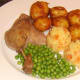 Duck leg is plated with roast potatoes and veg, ready for plum sauce