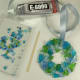 8. For the final touch add a few beads to your stunning piece. I first lay out all the beads that might work well with the colors of cobbles I have used. By placing the beads on a white paper plate or my favorite is to reuse a clam shell, you can eas