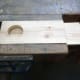 Placing one of the pieces of wood for the final stand underneath the prototype so as to give the hole cutter bit grip.