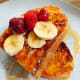Homemade Italian white bread French toast served with fresh sliced banana, raspberries, and maple syrup