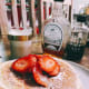 Homemade pancakes topped with fresh sliced strawberries and served with two types of maple syrup