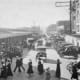 Scene in Pike Place Market c. 1915. Looking roughly northwest on Pike Place. At left, Main Market (later rebuilt as Main Arcade). At right, Corner Market and Sanitary Market. In distance, Washington National Guard Armory.