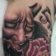 A blank-eyed hannya mask next to a flower.
