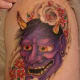 A colorful purple hannya mask tattoo with flowers.